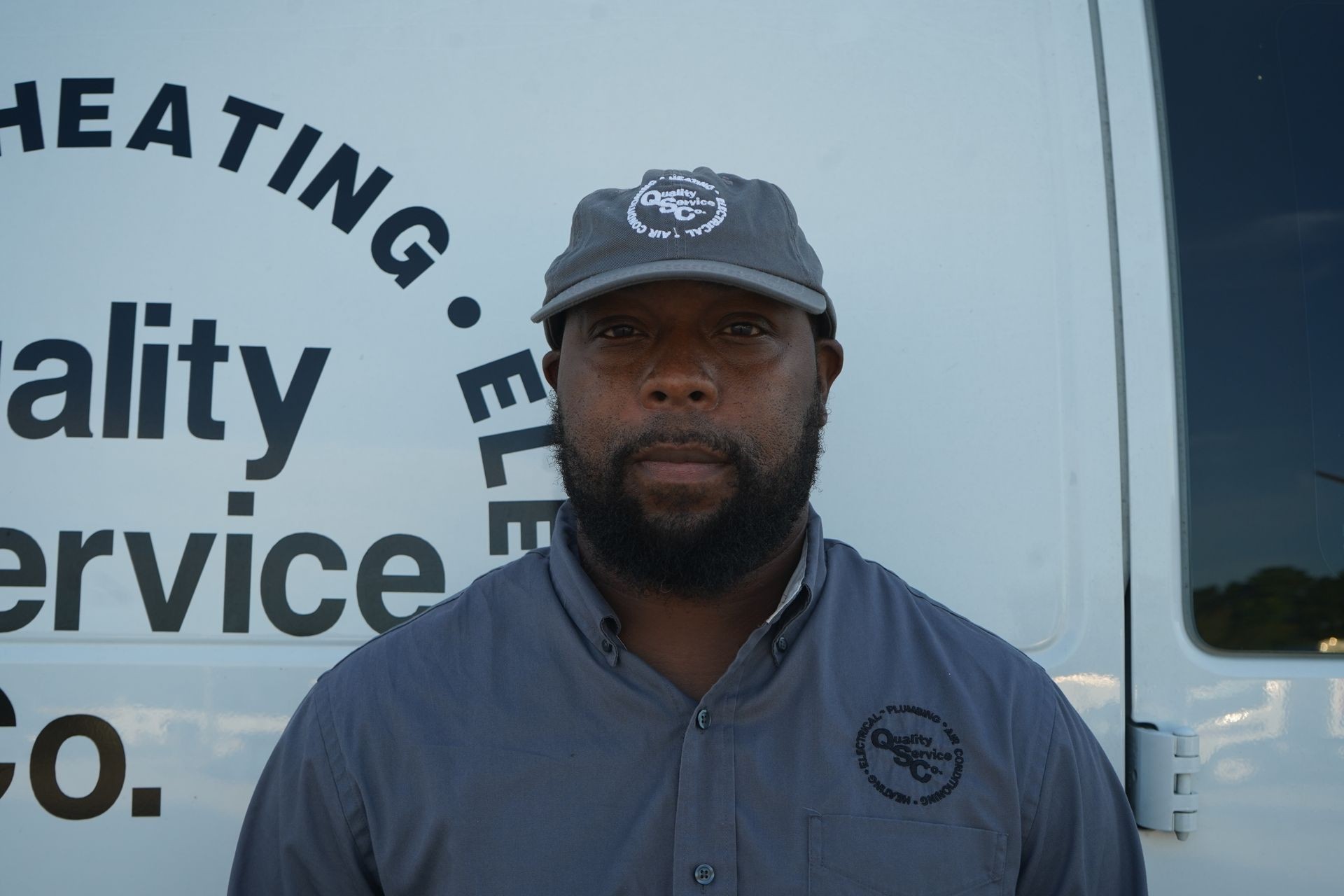 Man in a gray cap and shirt standing in front of a company van with service logos.