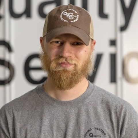 Person wearing a cap and gray shirt, standing in front of a blurred signboard with text.