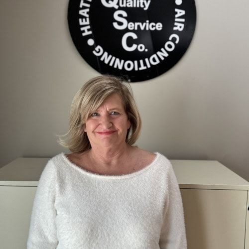 Woman in white sweater standing in front of a circular company sign on the wall.