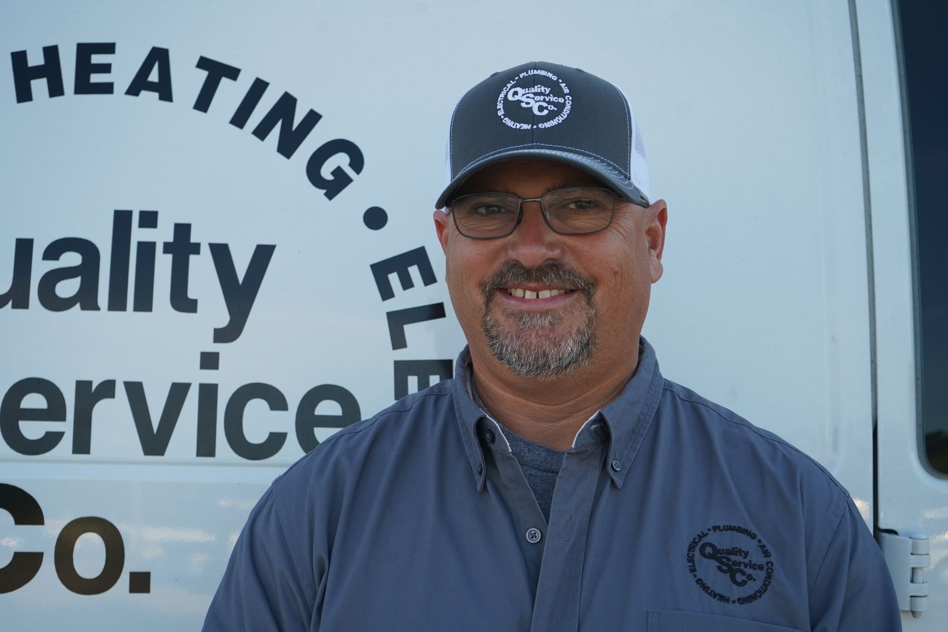 Smiling person in uniform and cap standing in front of a company van with business name signage.