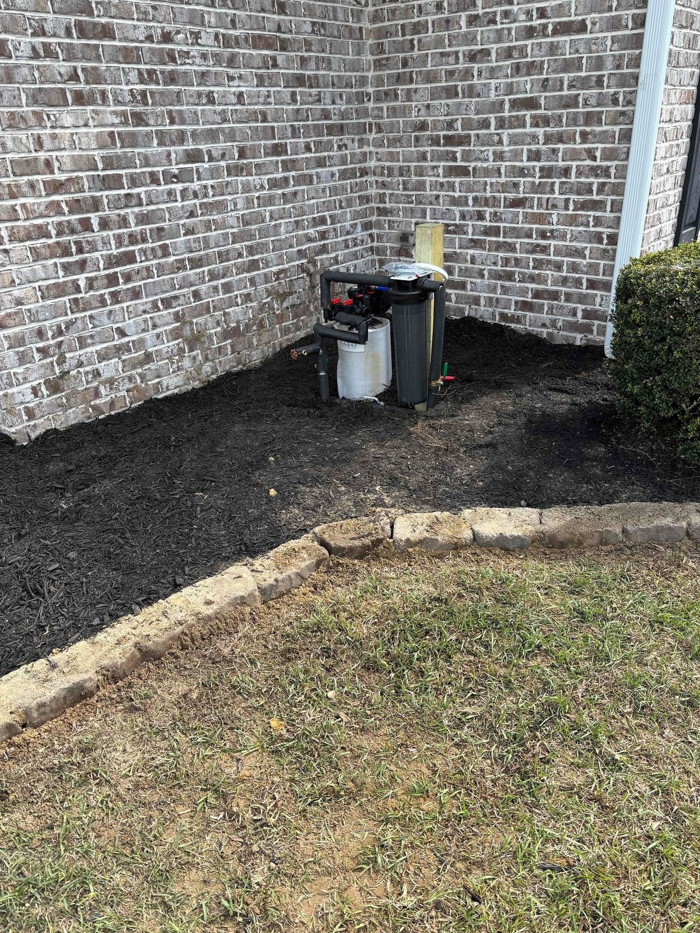 Water filtration system installed beside a brick house with dark mulch and a grassy area.