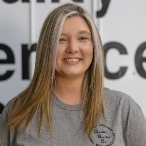 Woman with long hair smiling, wearing a gray T-shirt with company logo in a professional setting.