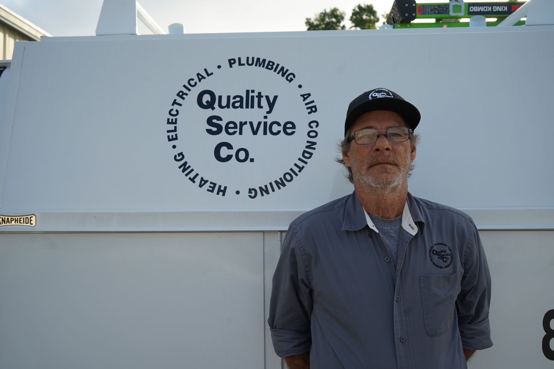 Man in work attire standing next to a service van with Quality Service Co. logo.