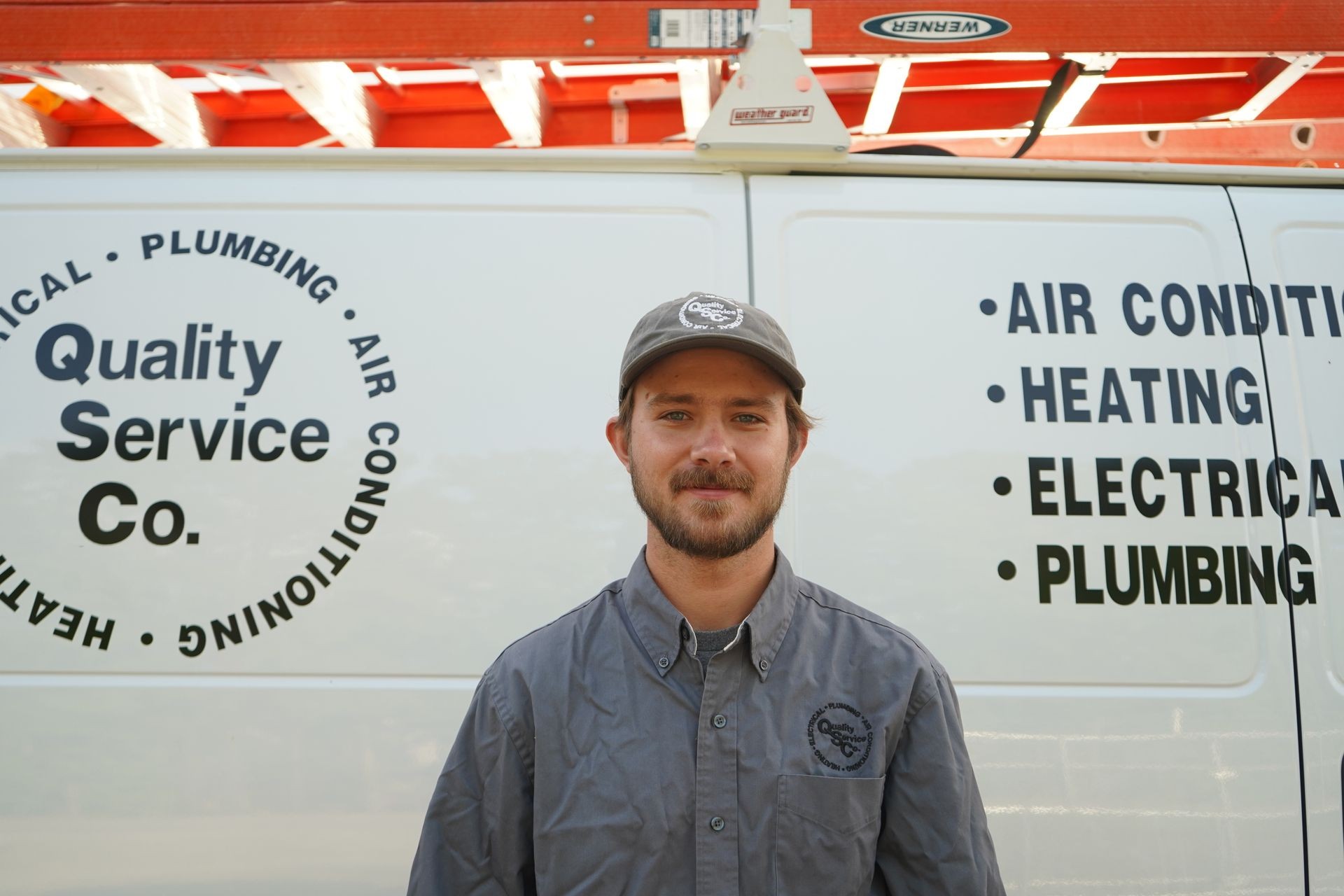 Service technician in uniform standing in front of a company van with service details printed on the side.