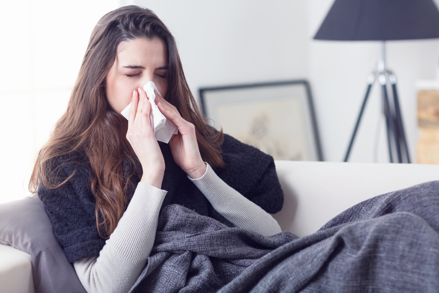 Woman blowing nose due to allergies from the poor indoor air quality in her home.