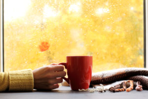 Woman drinking cup of coffee in front of fall window in her home enjoying her clean indoor air quality.