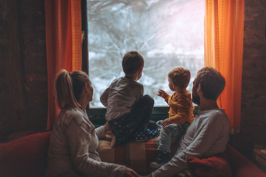 family keeping their heat and staying warm indoors and looking out the window of their home during winter's extreme cold weather.