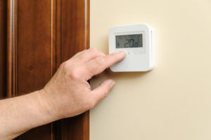 person's hand changing the temperature controls on a thermostat