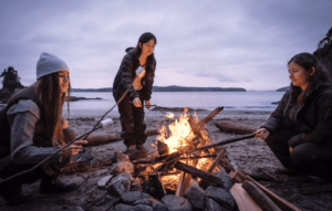 Women around campfire roasting marshmallows by the lake during winter