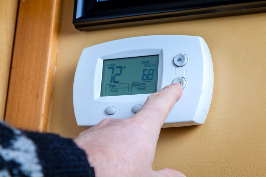 Should I Select “On” or “Auto” Fan Setting on My Thermostat? Photo of someone setting a thermostat that is mounted on a wall.